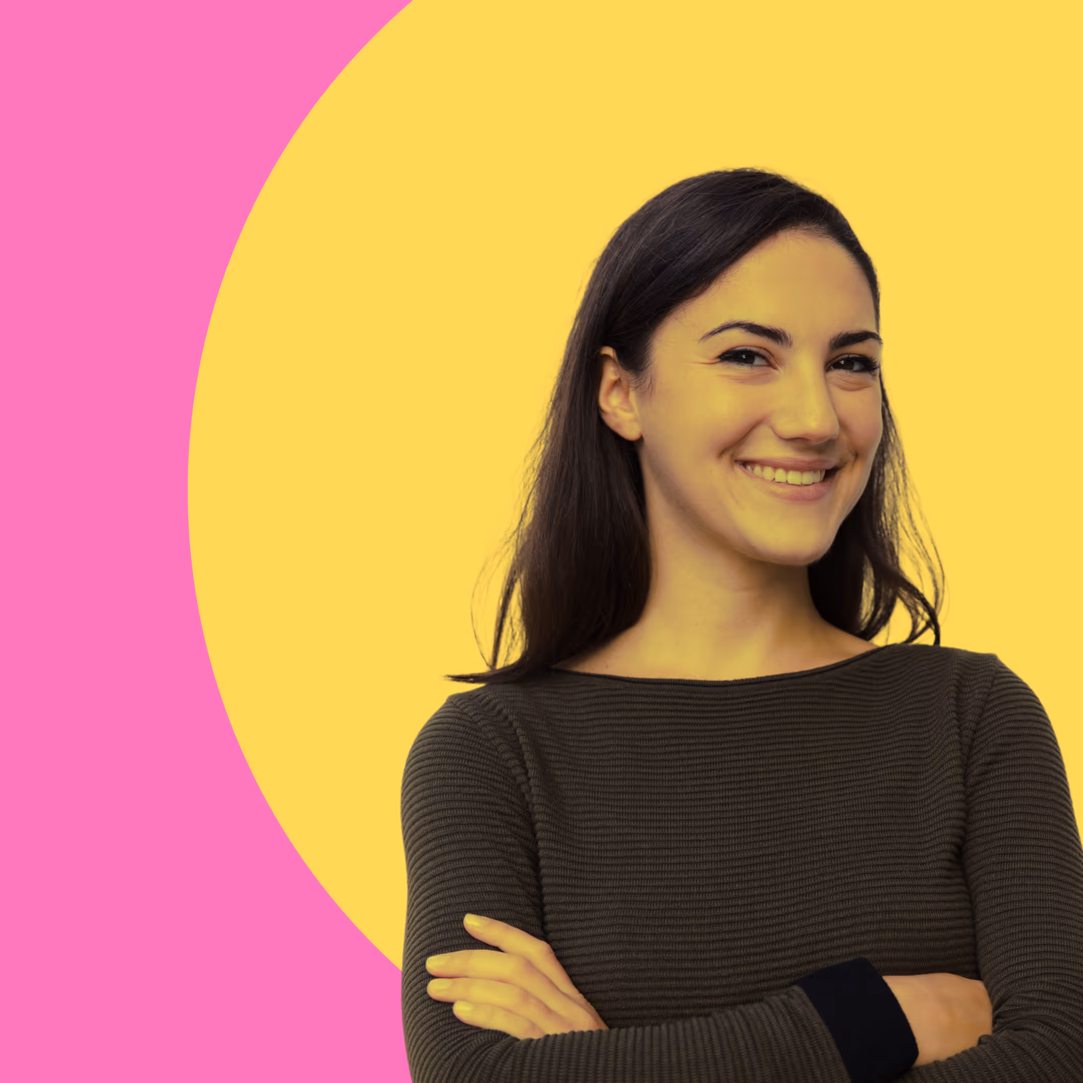 Junge Frau mit langen dunklen Haaren lächelt mit verschränkten Armen vor einem gelben und pinken Hintergrund.