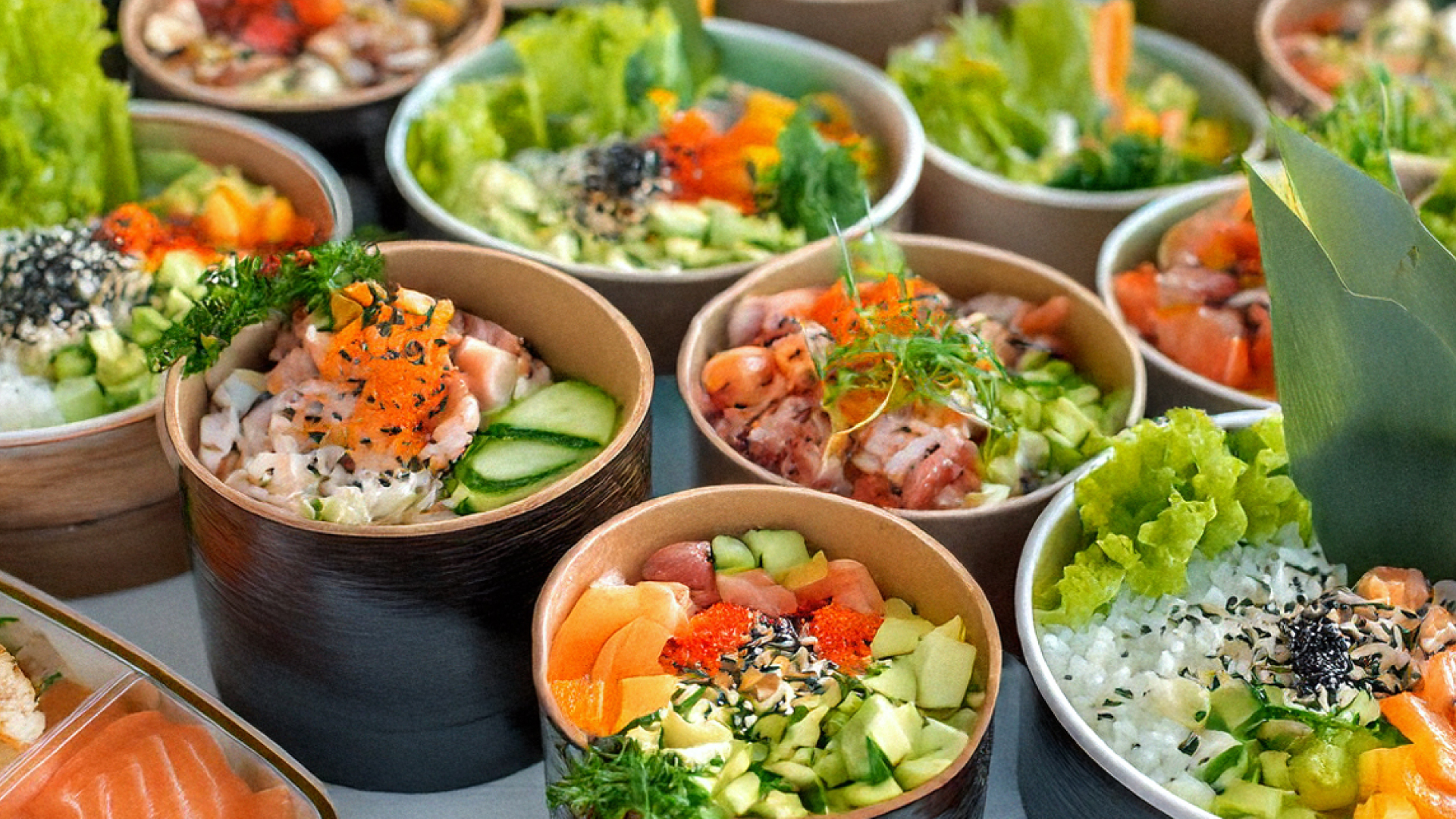Mehrere Schalen mit bunten Poke-Bowls, gefüllt mit rohem Fisch, Gurken, Salat und Sesam.