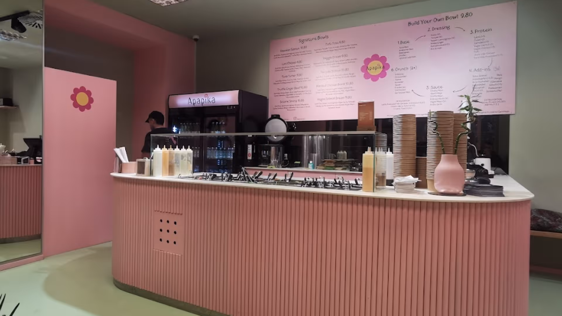 Theke eines pinkfarbenen Restaurants mit Menütafel im Hintergrund und verschiedenen Saucen und Besteck auf der Theke.
