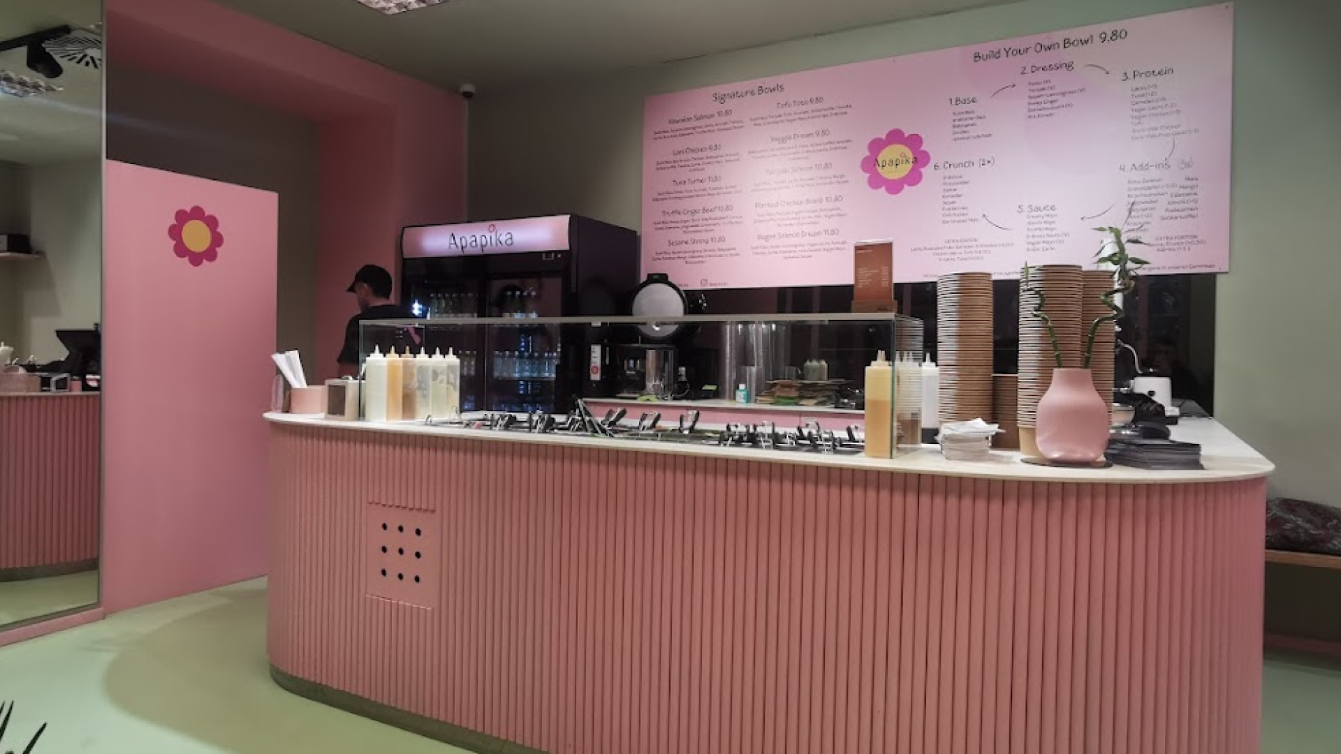 Theke eines pinkfarbenen Restaurants mit Menütafel im Hintergrund und verschiedenen Saucen und Besteck auf der Theke.