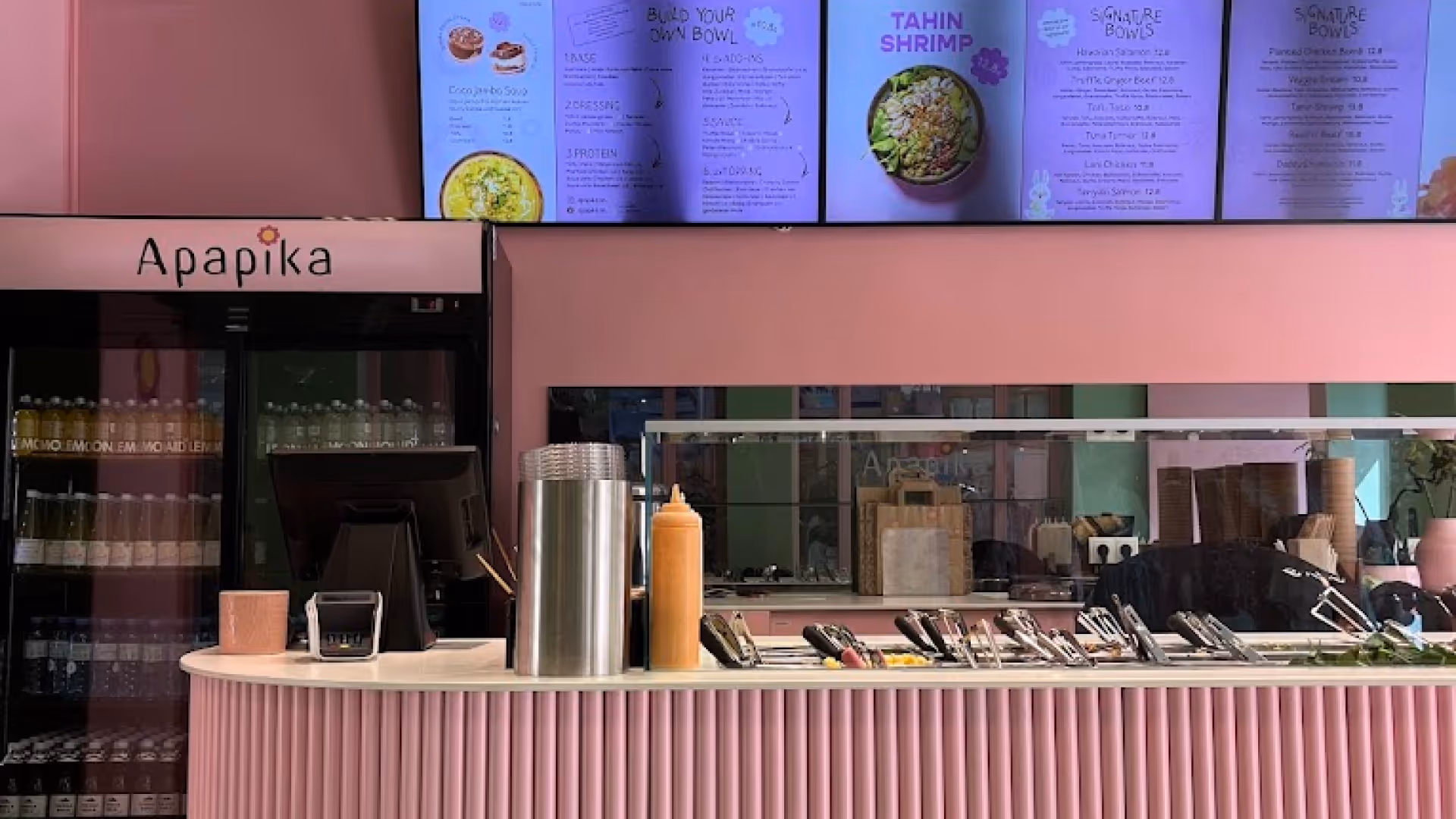 Blick auf die Theke eines modernen, rosa gestalteten Restaurants namens Apapika mit digitaler Speisekarte und Menüelementen zur Selbstgestaltung von Schalen.