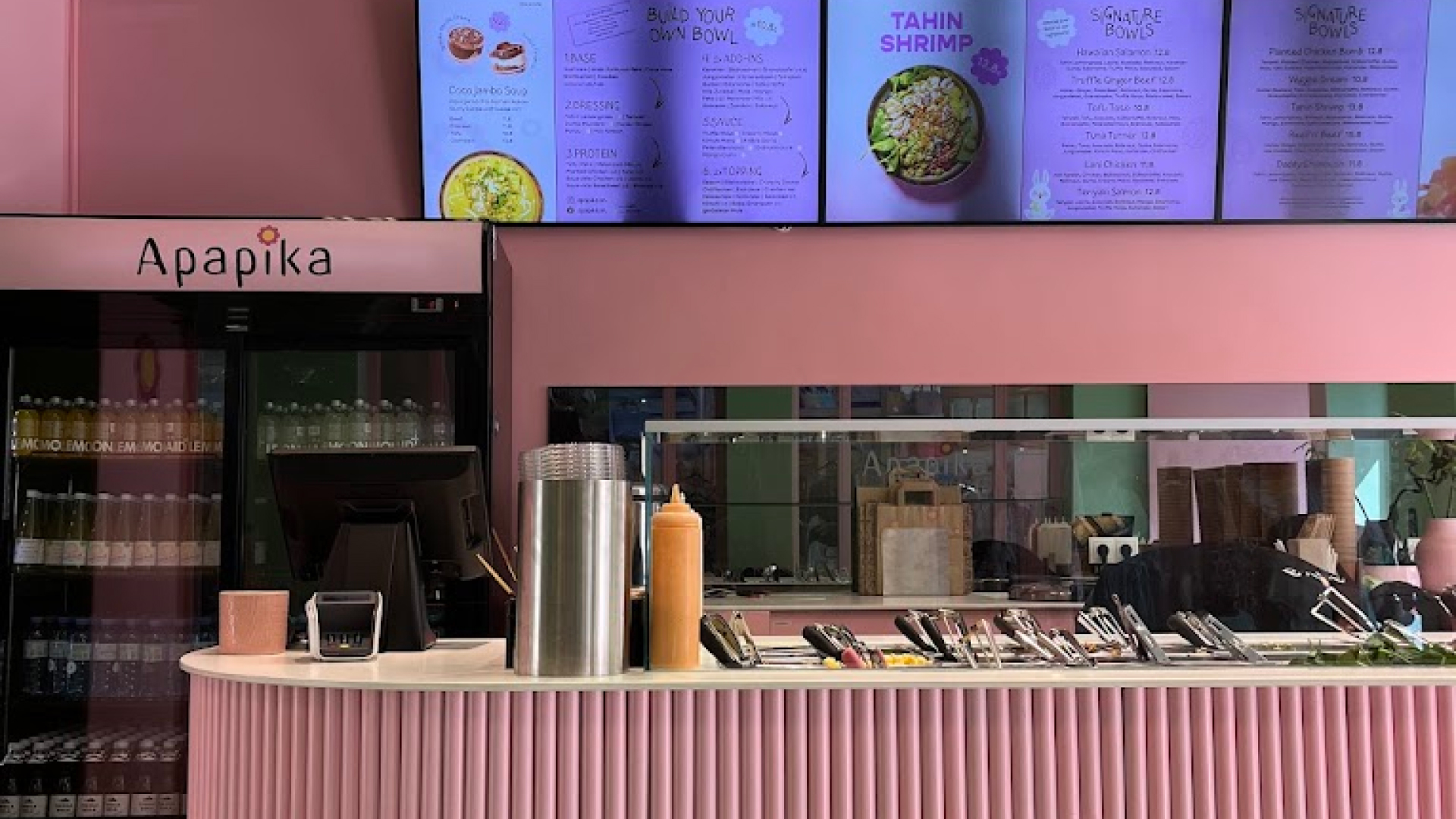 Blick auf die Theke eines modernen, rosa gestalteten Restaurants namens Apapika mit digitaler Speisekarte und Menüelementen zur Selbstgestaltung von Schalen.