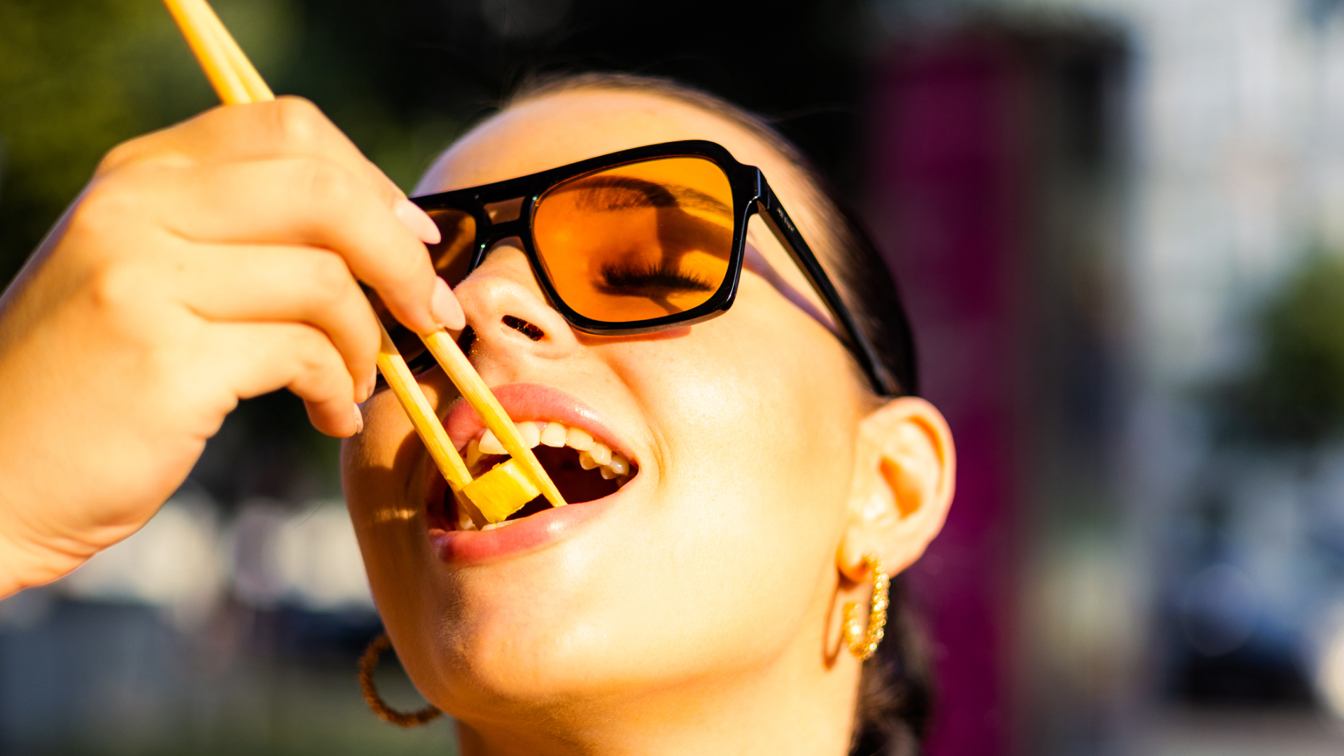 Frau mit orangen Sonnenbrillen, die ein Stück für Sushi mit Essstäbchen isst.