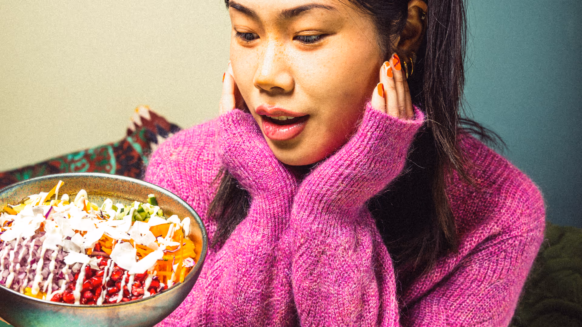 Frau in rosa Pullover bewundert eine bunte Salatschüssel mit verschiedenen Gemüsesorten und Dressing.