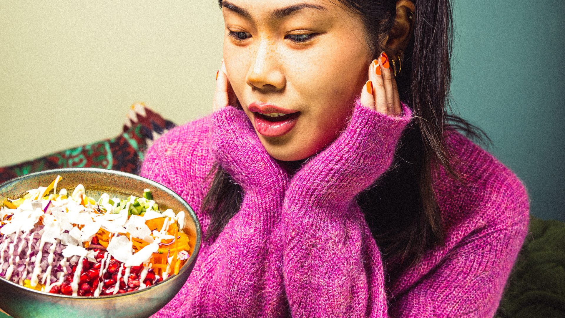Frau in rosa Pullover bewundert eine bunte Salatschüssel mit verschiedenen Gemüsesorten und Dressing.
