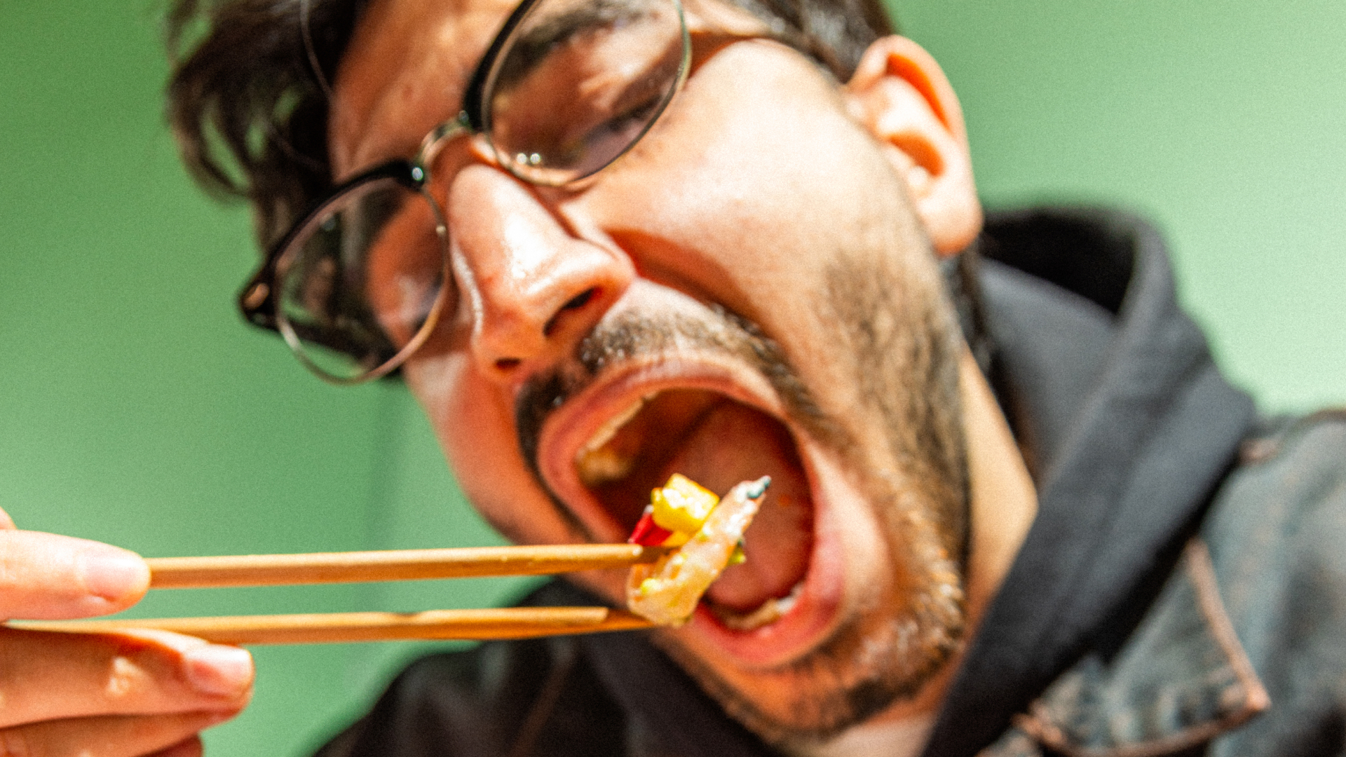 Nahaufnahme eines Mannes mit Brille, der mit Chopsticks ein Stück Sushi isst.
