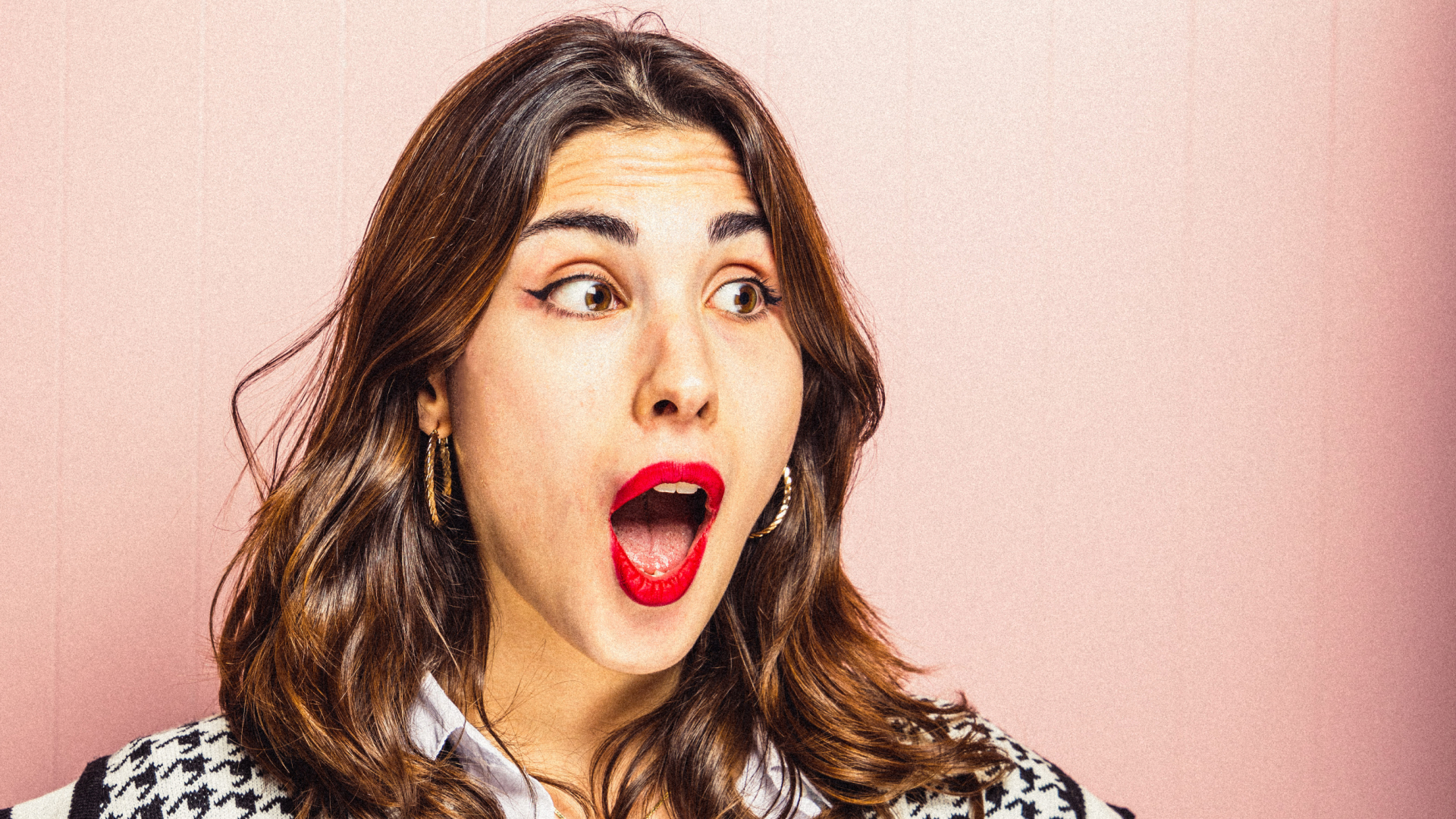 Frau mit roten Lippen und braunen Haaren, die überrascht mit offenem Mund nach rechts schaut.