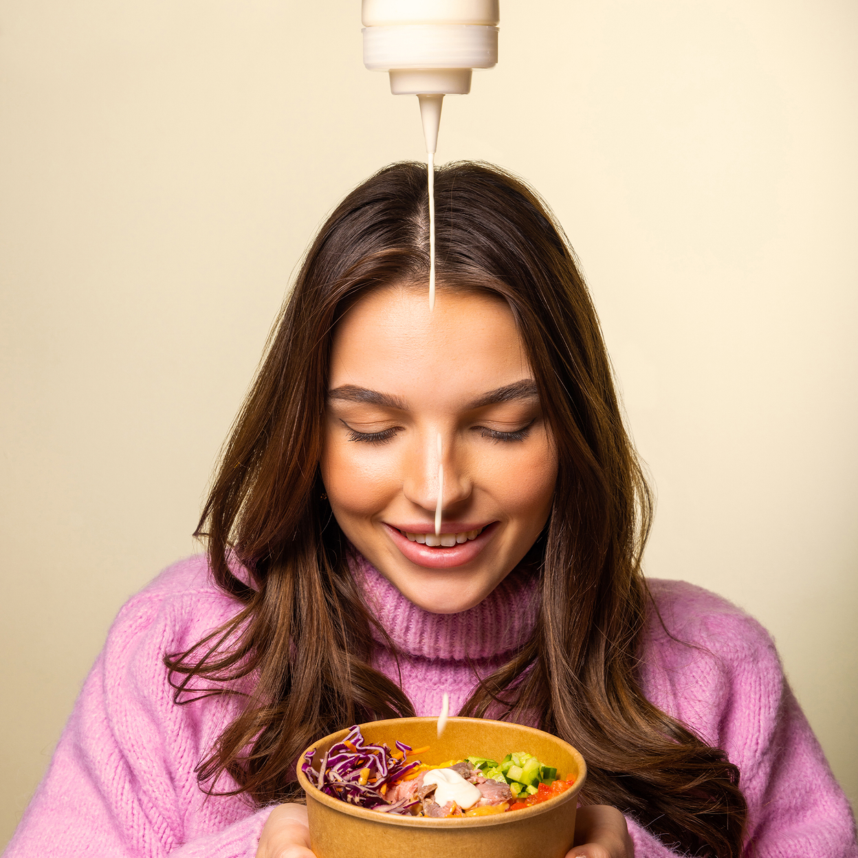 Junge Frau gießt cremiges Dressing auf eine Schüssel mit frischem Salat und Gemüse.