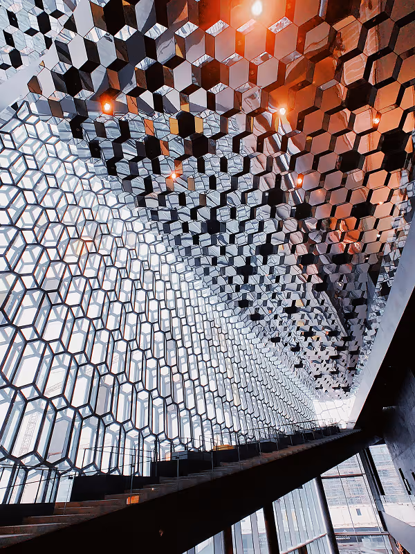 Intérieur d'un bâtiment moderne avec une grande façade en verre à motifs hexagonaux et un plafond en miroirs.
