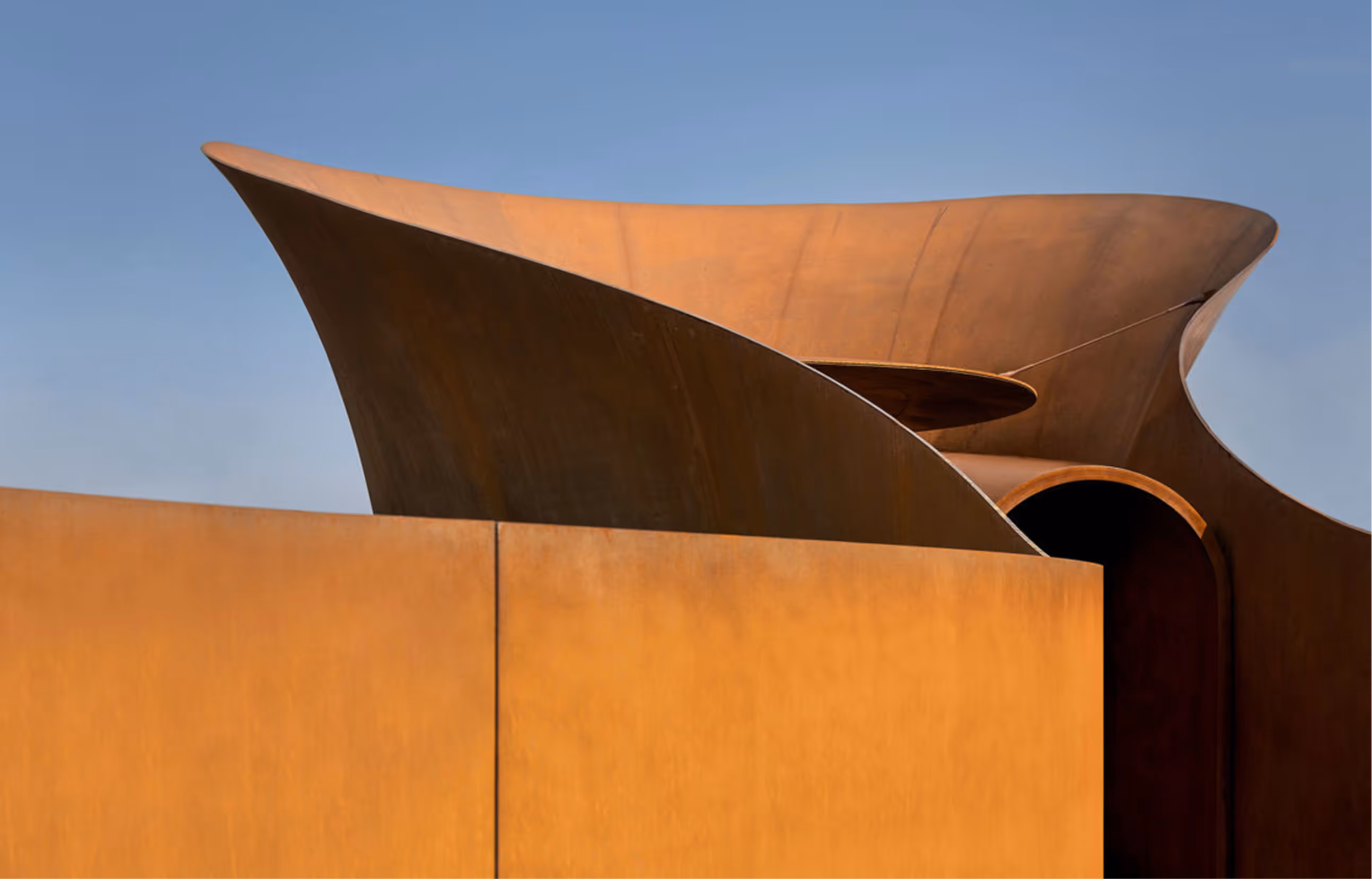 Structure métallique rouillée avec des formes incurvées sous un ciel bleu clair.