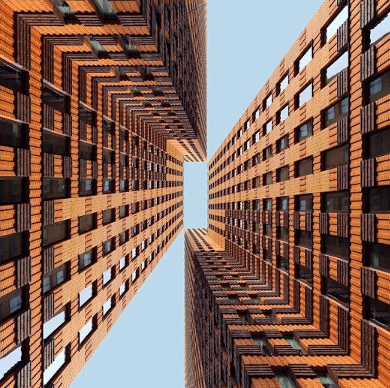 Vue en contre-plongée de deux immeubles en briques rouges se faisant face avec un ciel clair entre eux.