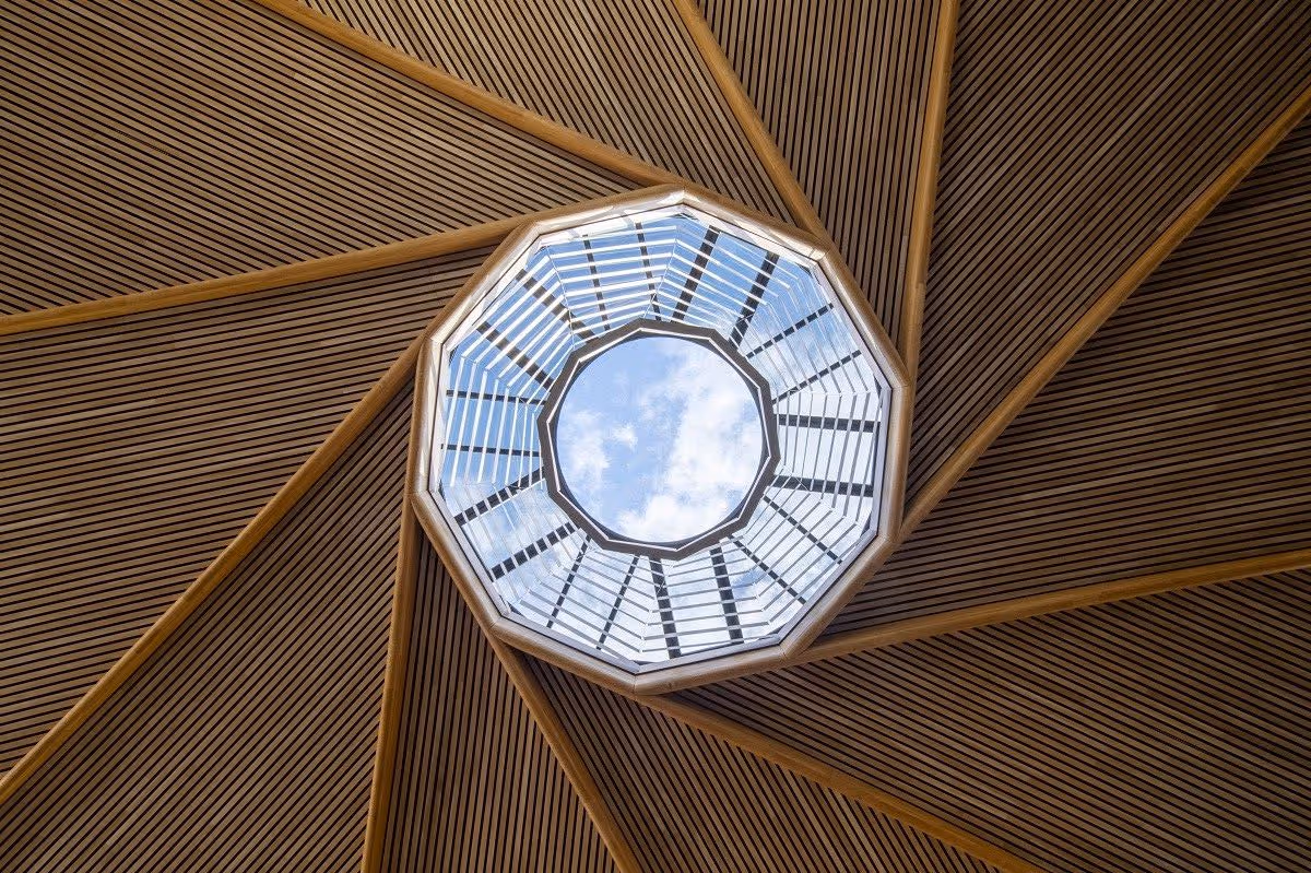 Plafond en bois avec un puits de lumière octogonal affichant un ciel bleu avec des nuages.