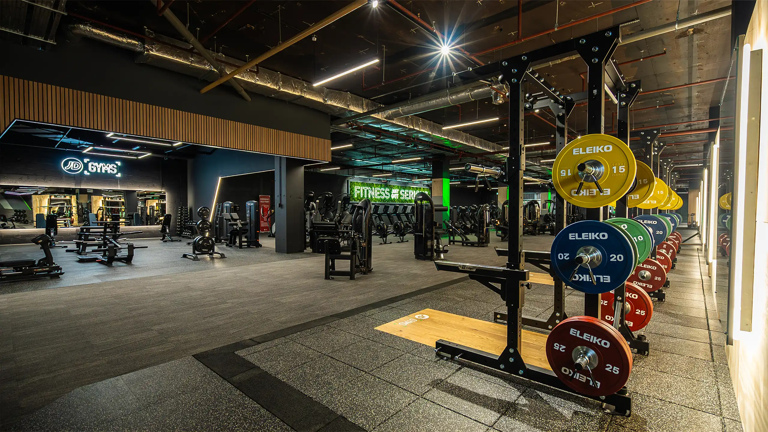 Modern gym interior with weightlifting racks holding colorful Eleiko weight plates and various fitness machines in the background.