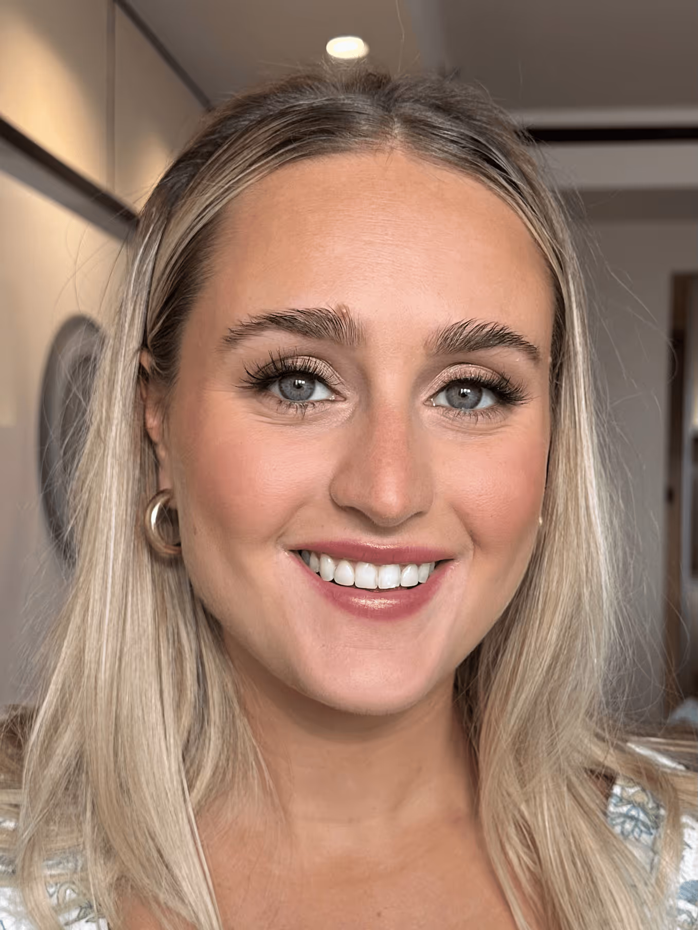 Close-up portrait of a smiling woman with long blonde hair, blue eyes, and gold hoop earrings.