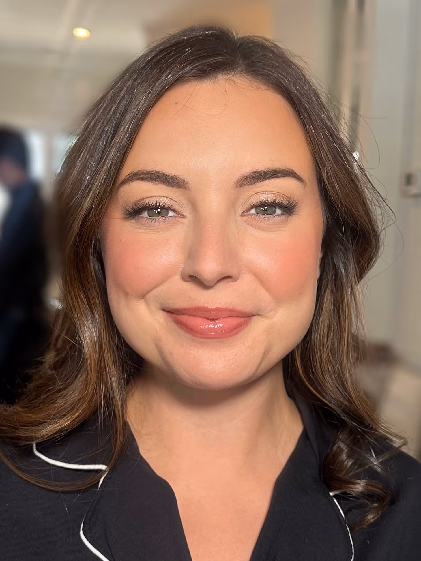 Close-up of a smiling woman with long brown hair, wearing a black top with white piping.