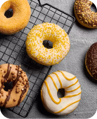 Variety of five donuts with different icings and toppings placed on and around a black cooling rack on a gray surface.