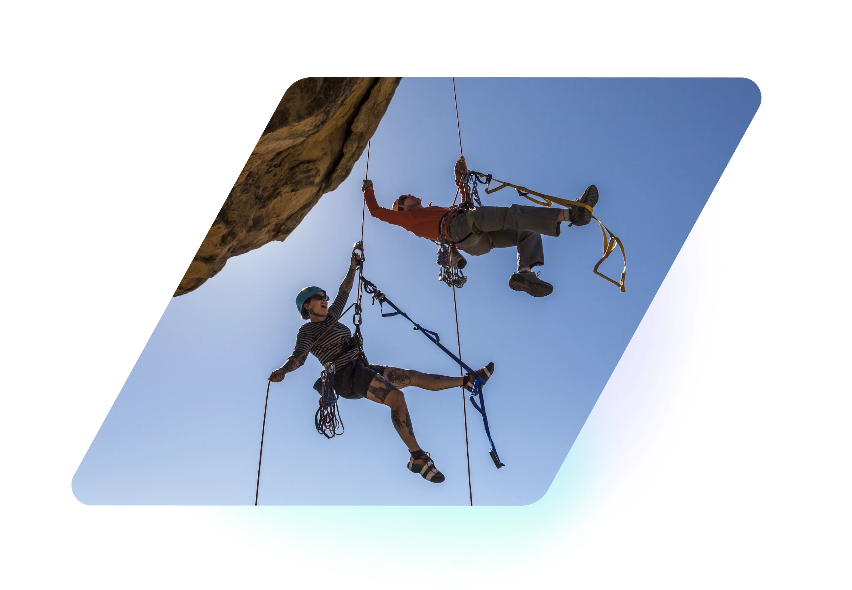 Two rock climbers suspended on ropes against a clear blue sky, climbing an overhanging rock.