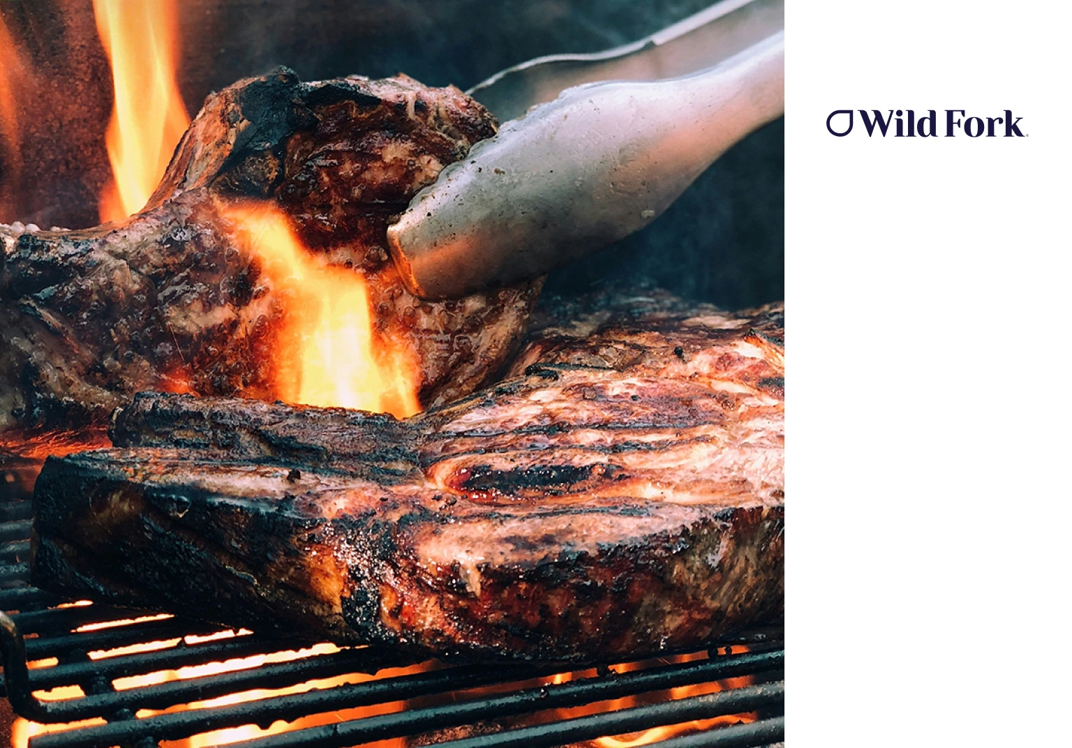 Close-up of juicy steaks being grilled over open flames with metal tongs holding one steak.