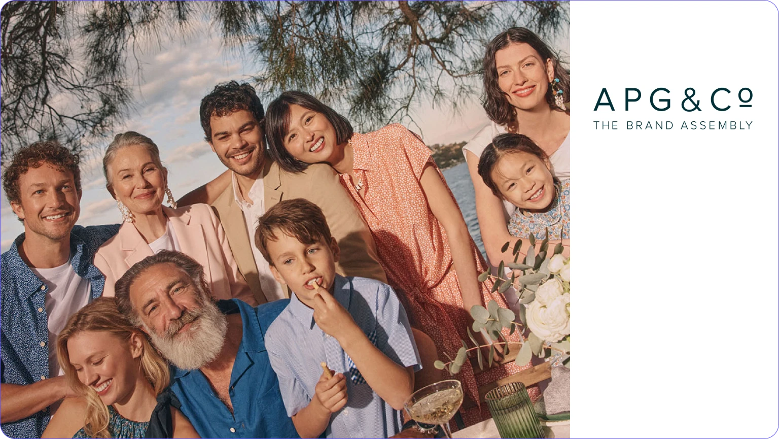 Group of diverse smiling people posing together outdoors with trees and water in the background.