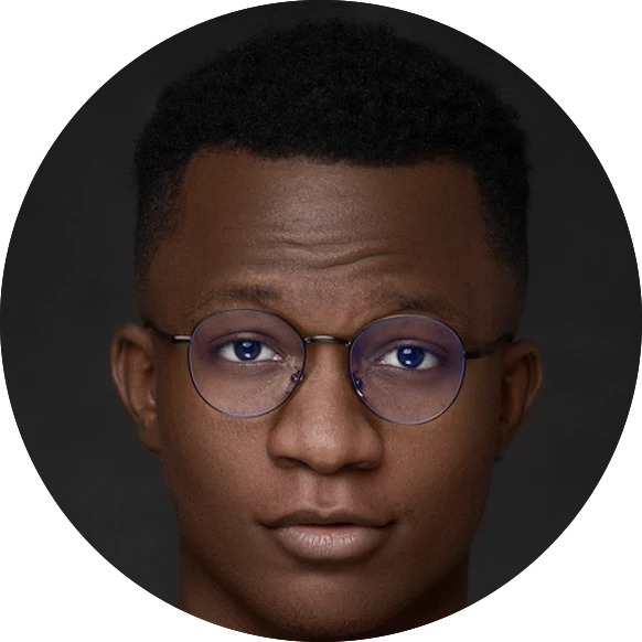 Close-up portrait of a man with short hair wearing round glasses and looking directly at the camera against a dark background.