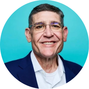 Smiling middle-aged man with short gray hair, glasses, wearing a navy suit and white shirt against a blue background.