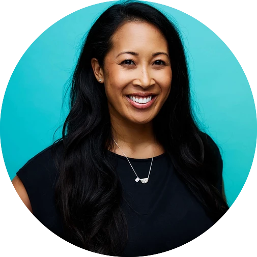 Smiling woman with long black hair wearing a black top and silver necklace against a turquoise background.