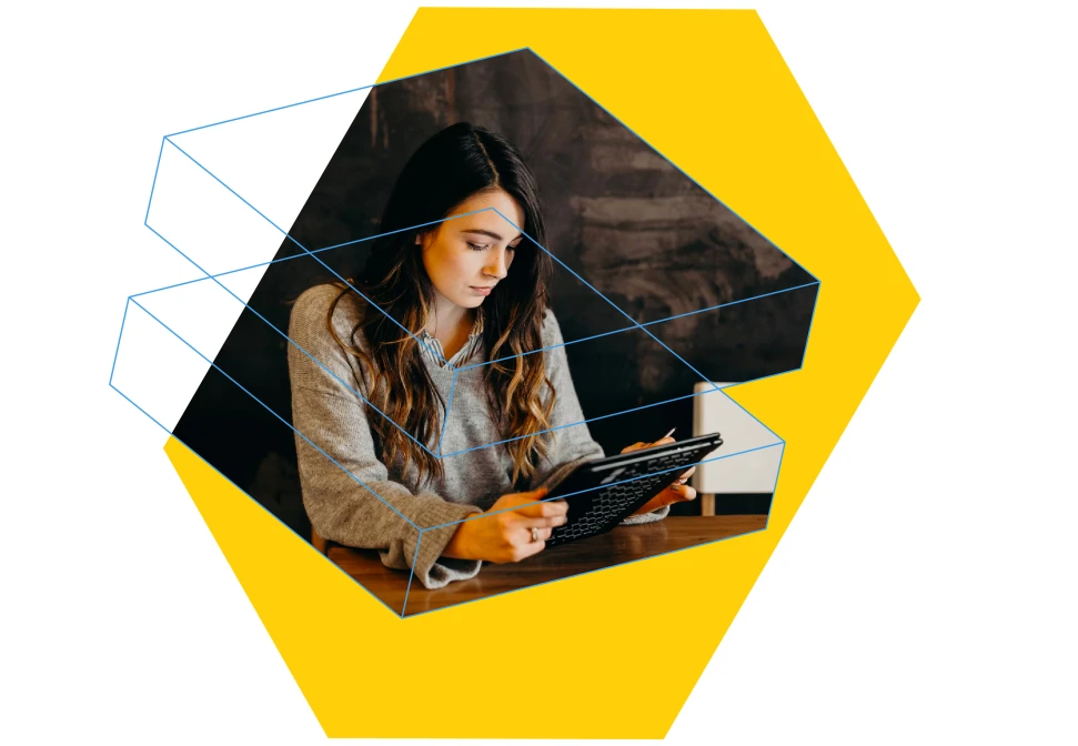 Woman with long hair wearing a gray sweater, using a digital tablet over a wooden table with a dark background and yellow hexagonal overlay.