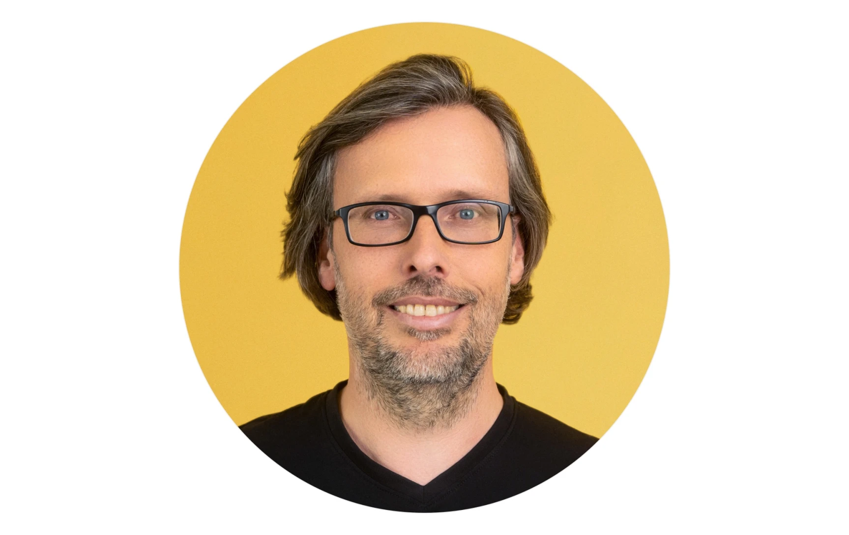 Middle-aged man with glasses, short graying hair, and beard smiling against a yellow background.