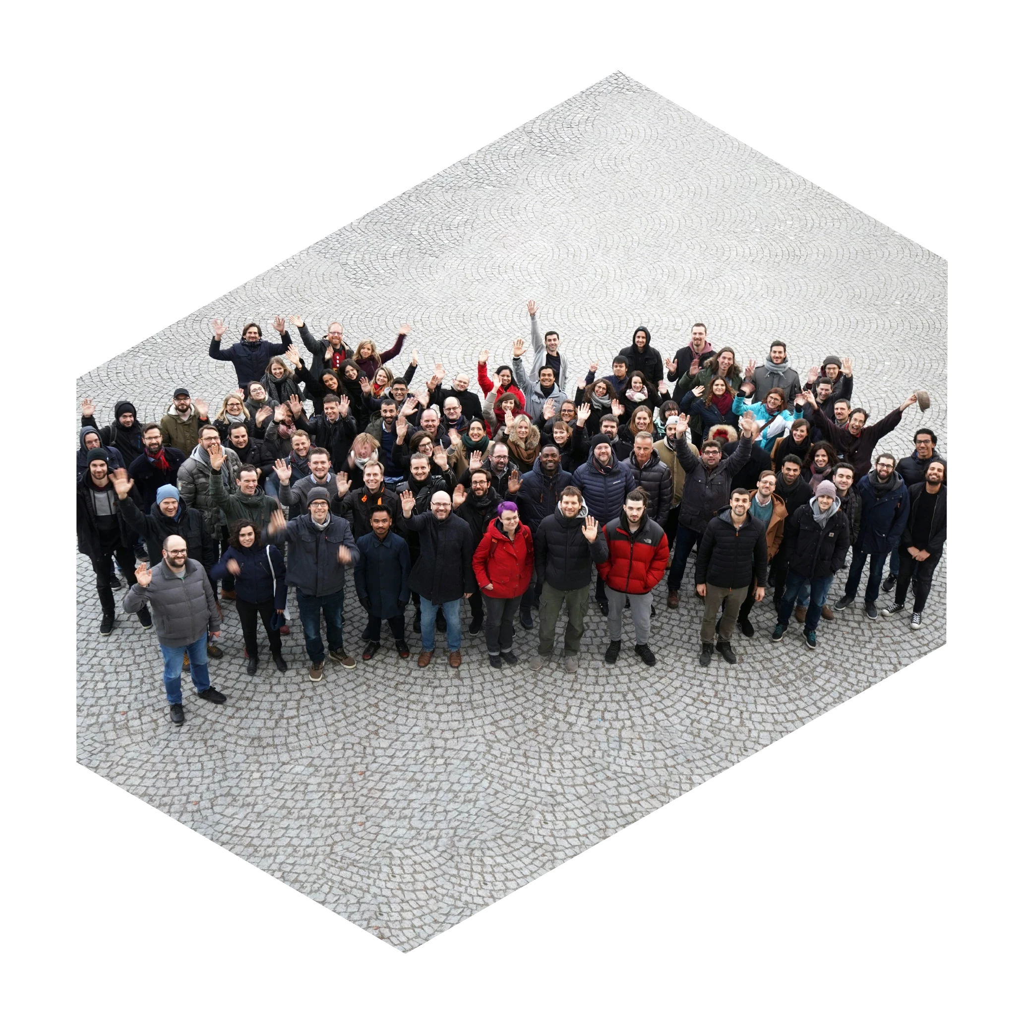Large group of diverse people standing on stone pavement waving and smiling at the camera.