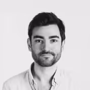 Black and white headshot of a man with dark hair, a trimmed beard, and wearing a light-colored shirt against a plain background.