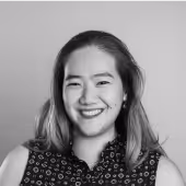 Smiling woman with shoulder-length hair wearing a patterned sleeveless top against a plain background.