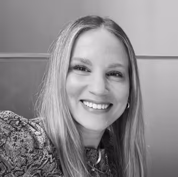 Smiling woman with long straight hair wearing a patterned top and hoop earrings.