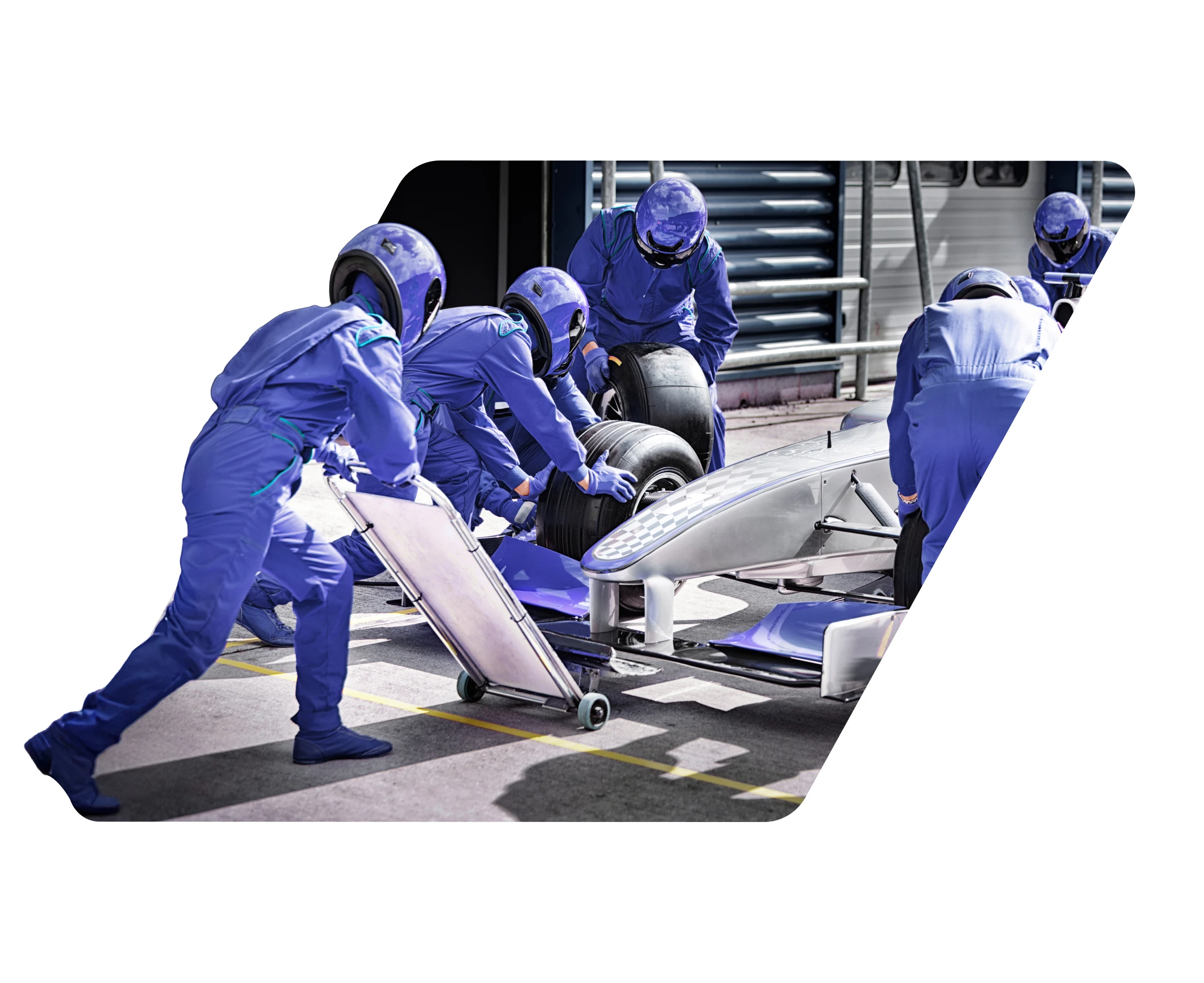 Pit crew in blue suits and helmets changing tires on a silver race car during a pit stop.