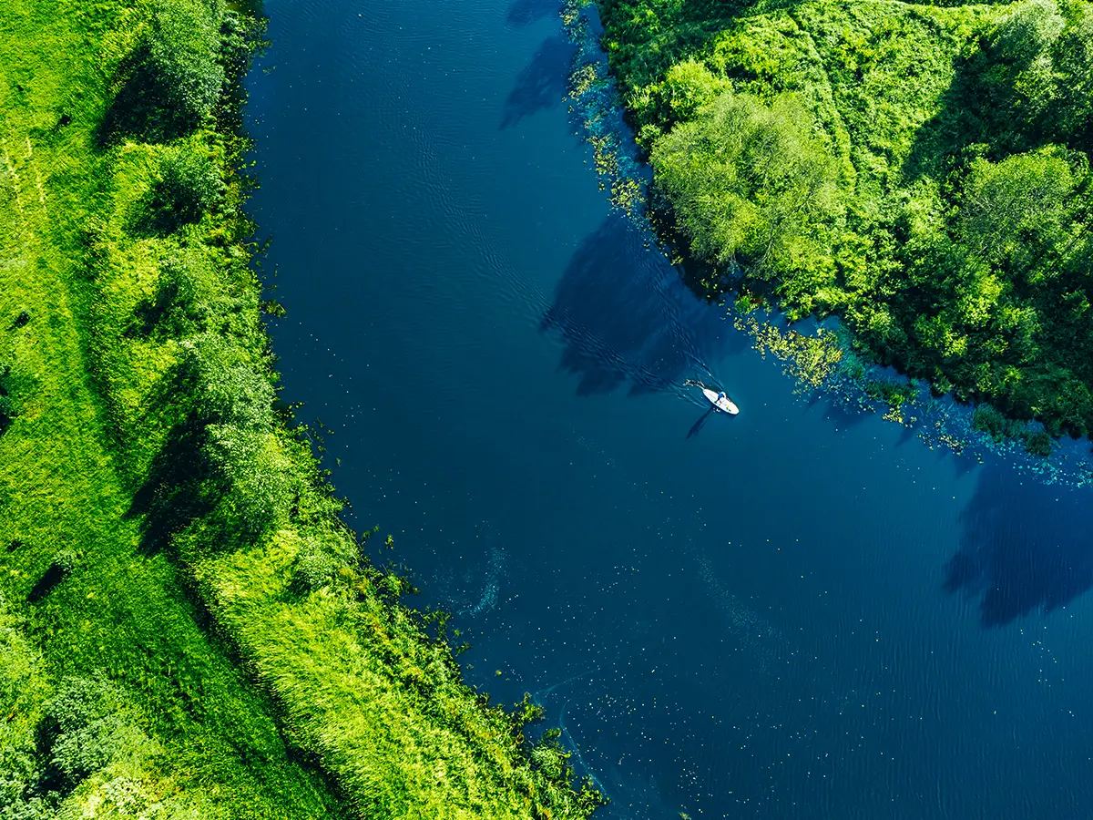 Aerial view of a person rowing a small boat on a blue river surrounded by lush green vegetation.
