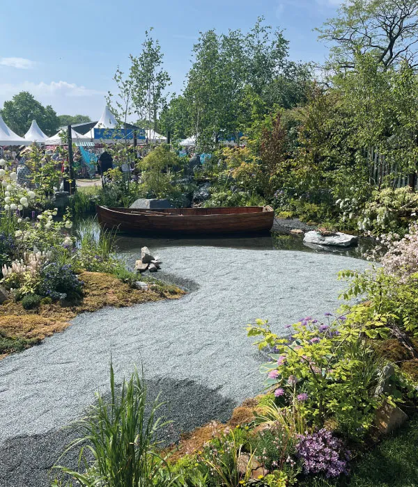 Wooden rowboat resting in a small pond surrounded by lush greenery and flowering plants at an outdoor garden event.