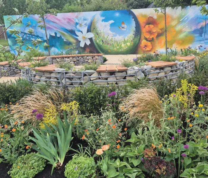 Colorful garden with blooming flowers, circular stone seating, and a vibrant mural of flowers and a butterfly on a wall.