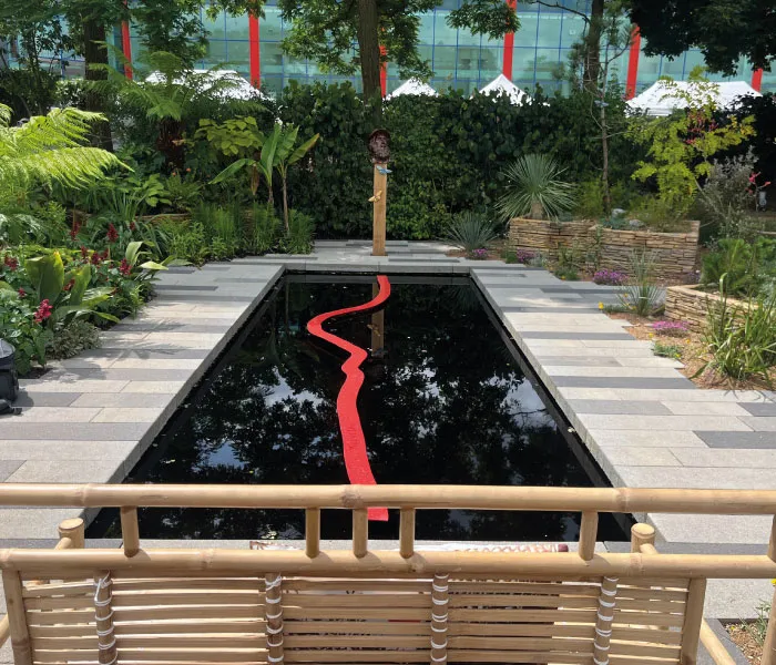 Reflective rectangular black pool with a red wavy line running through it, surrounded by greenery and stone pavement.