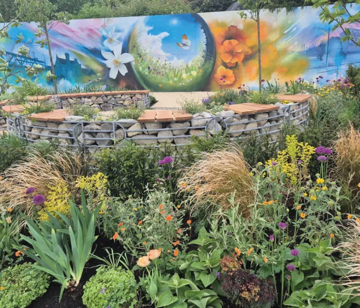 Colorful garden with vibrant wildflowers in front of a mural featuring large flowers, grass, and a butterfly.