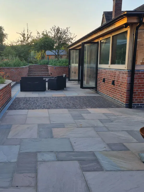 Outdoor patio with stone tile flooring, black seating, brick walls, and steps leading to a garden area.