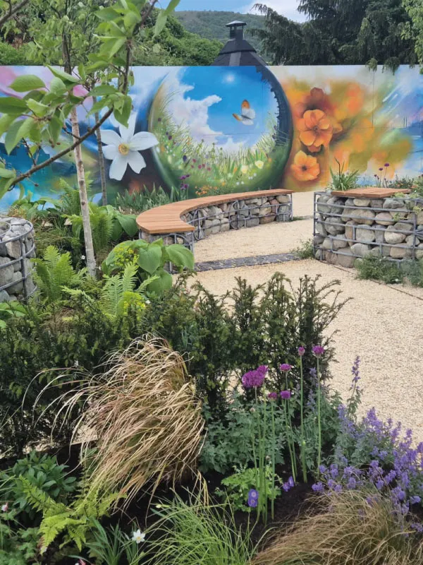 Garden with circular stone benches, lush plants, and a mural of flowers and a butterfly on the background wall.