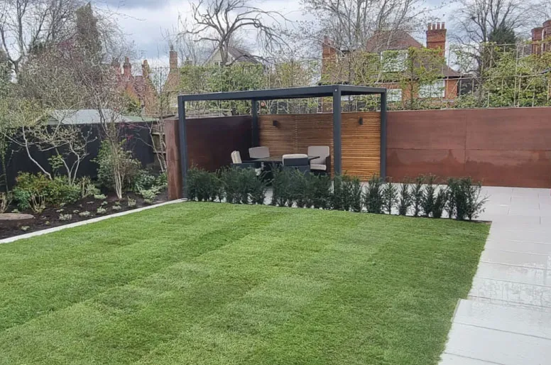 Modern garden with green lawn, paved patio, small hedges, and a seating area under a black pergola.