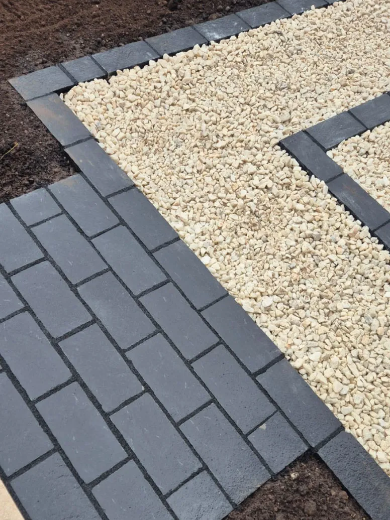 Close-up of a garden pathway with dark gray rectangular paving stones and adjacent beige gravel bordered by bricks.