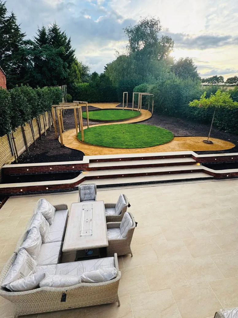 Modern backyard patio with light stone tiles, cushioned outdoor seating, and circular grass and path garden design.