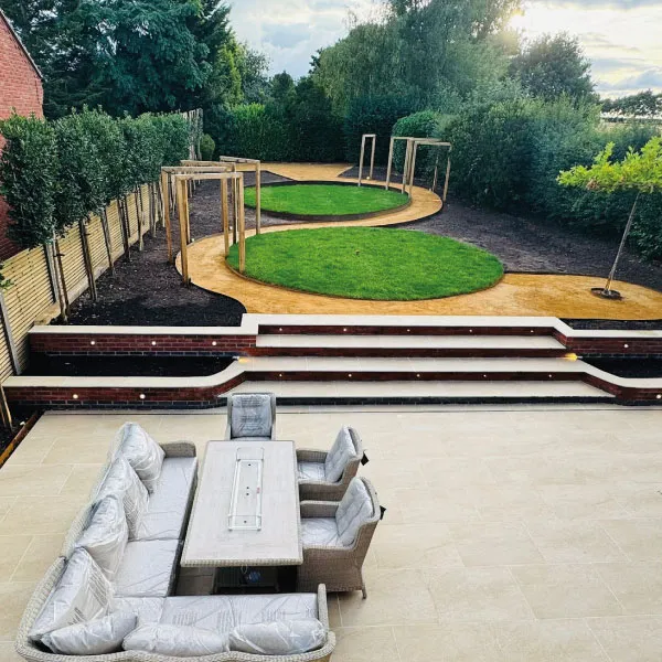 Modern garden with curved paths, circular grass areas, wooden pergolas, and a patio with cushioned outdoor seating and table.