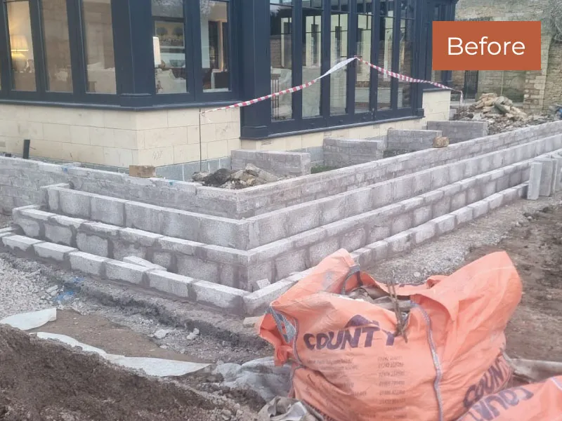 Unfinished garden wall construction in progress with stacked concrete blocks and building materials nearby.