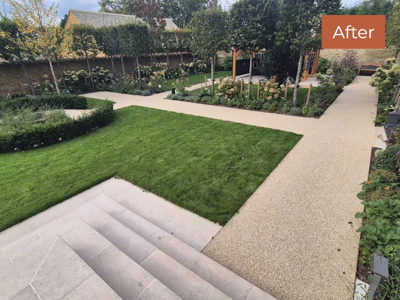 Neatly landscaped garden with green lawn, light stone steps, and gravel paths bordered by shrubs and trees.