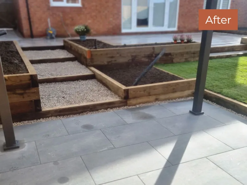 Patio with large gray tiles, wooden raised garden beds, gravel path, and artificial grass area in a backyard.