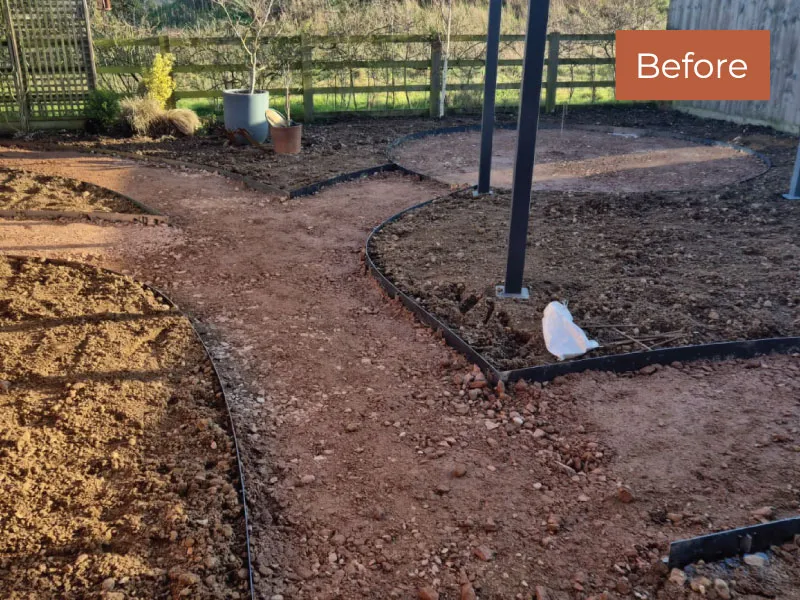 Unfinished garden path with exposed soil and gravel edged with black plastic borders under sunlight.