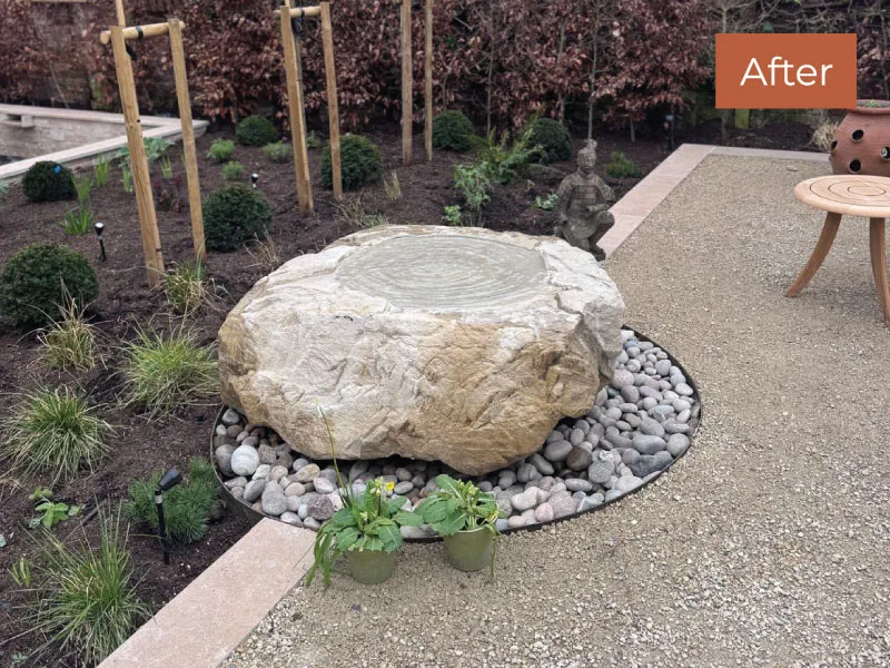 Large decorative stone water feature surrounded by pebbles in a landscaped garden area.