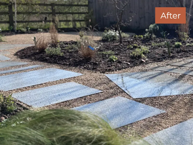 Outdoor garden path with evenly spaced rectangular stone slabs set in gravel surrounded by plants and fencing.
